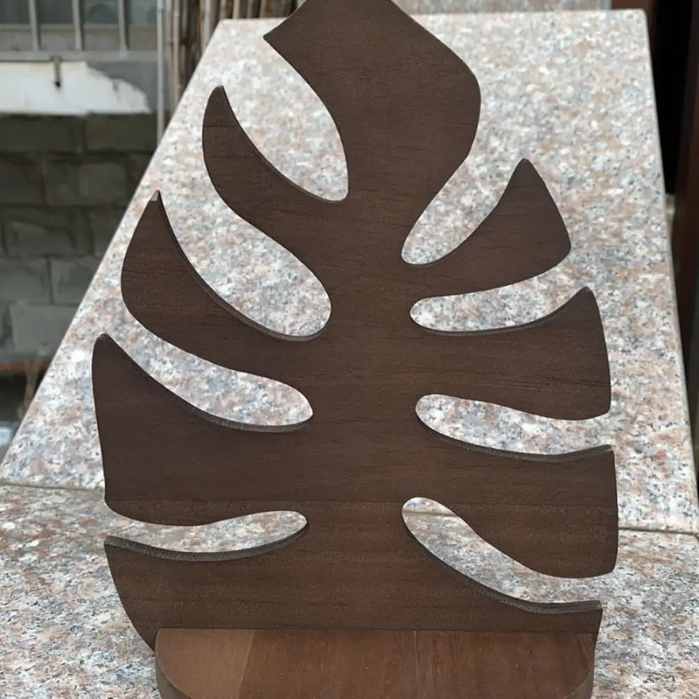 A dark brown wooden wall art frame shaped like a monstera leaf mounted on a light granite surface.