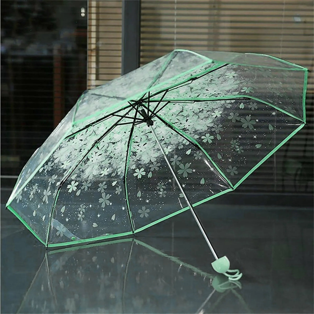 Ein klarer Regenschirm mit Blumenmuster liegt auf einer reflektierenden Oberfläche.
