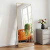 Ein vollflächiger Spiegel mit goldenem Rahmen reflektiert einen orangen Sessel und ein Fenster.