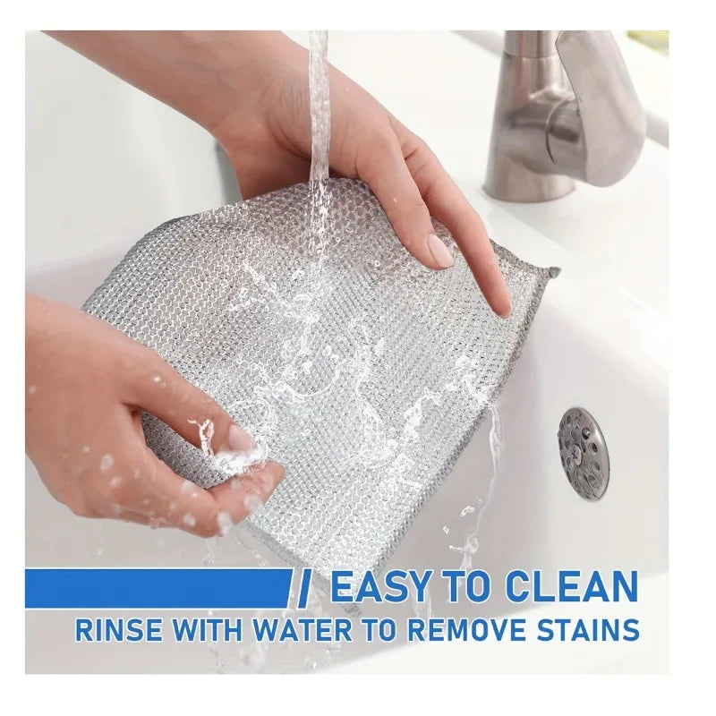 Hands are rinsing a square metal wire cleaning cloth under running water to remove stains.