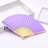 Un éventail pliable violet à la main fait de bambou et de papier, exposé sur une boîte blanche.