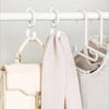 A light beige rotating closet organizer hook system mounted on a white bar, with a cream-colored bag and a pink garment hangi