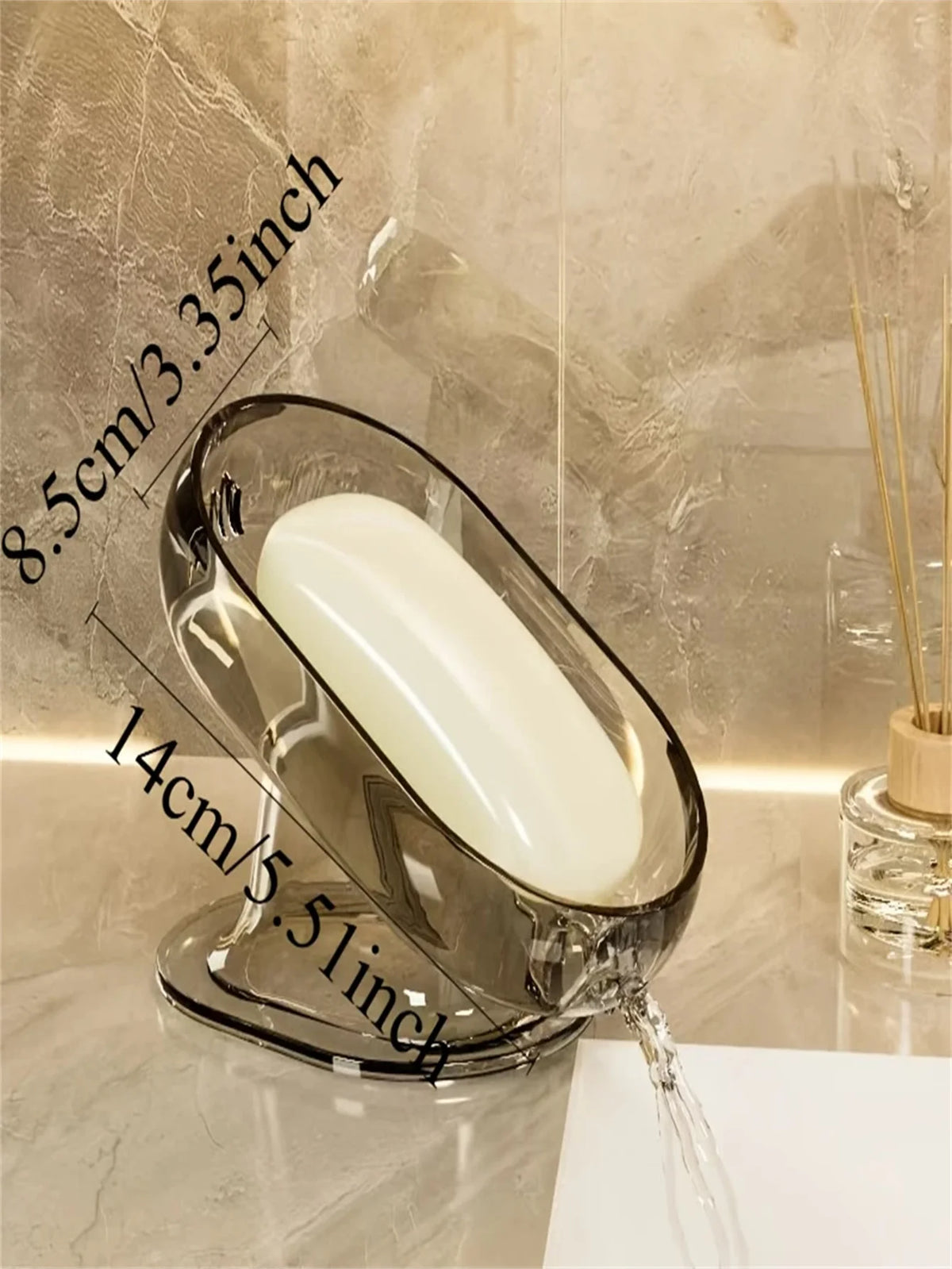 A clear glass soap dish with a white bar of soap is shown on a marble surface.