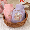 Two plush cartoon hot water bottles, one pink and one purple, are shown in a woven basket.