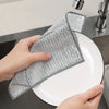 A hand is placing a silver wire cleaning dish rag onto a white plate in a kitchen sink.