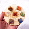 A hand holds a wooden circle containing several natural stone pyramid crystals arranged in a geometric pattern.