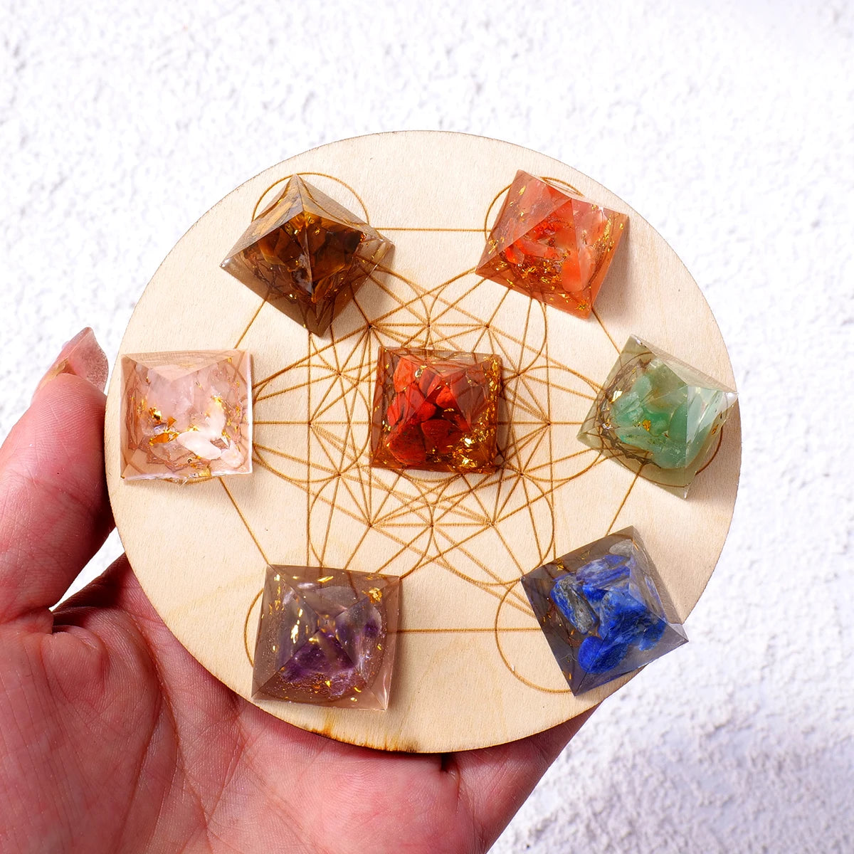 A hand holds a wooden circle containing several natural stone pyramid crystals arranged in a geometric pattern.