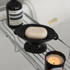A black ceramic double-ear soap dish holding a beige bar of soap next to an Aesop bottle on a wire rack.