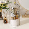 A clear spherical organizer for makeup brushes with a gold lid and white base on a light surface.