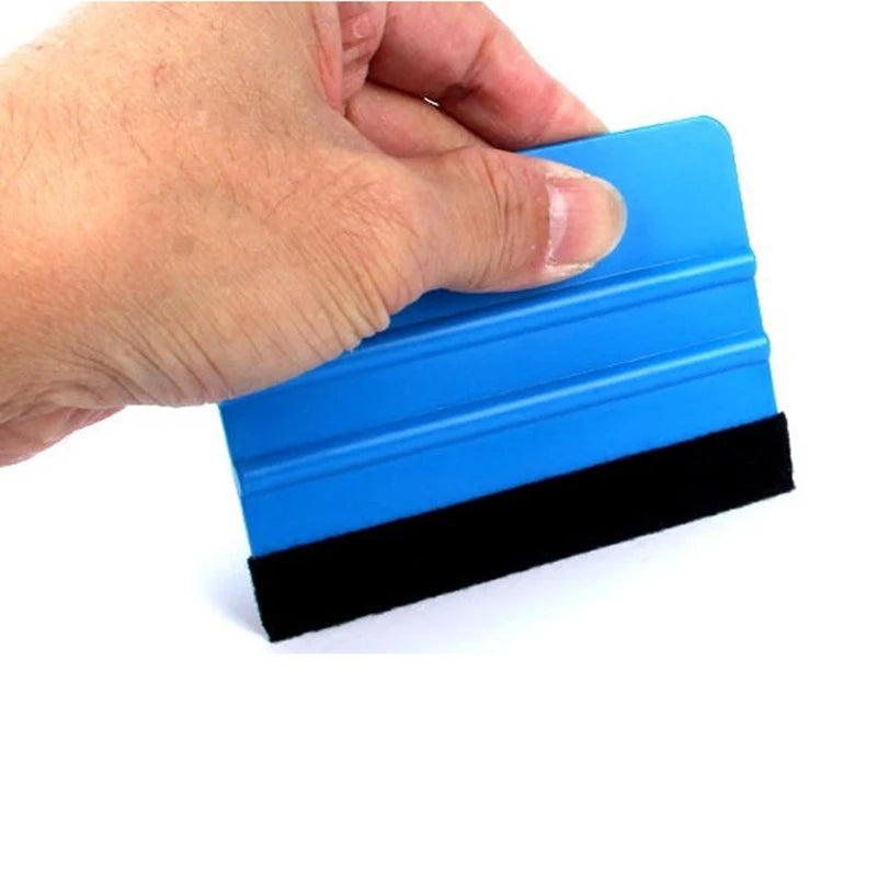 A hand is holding a blue suede felt squeegee with a black rubber blade for vinyl wrap and film installation.
