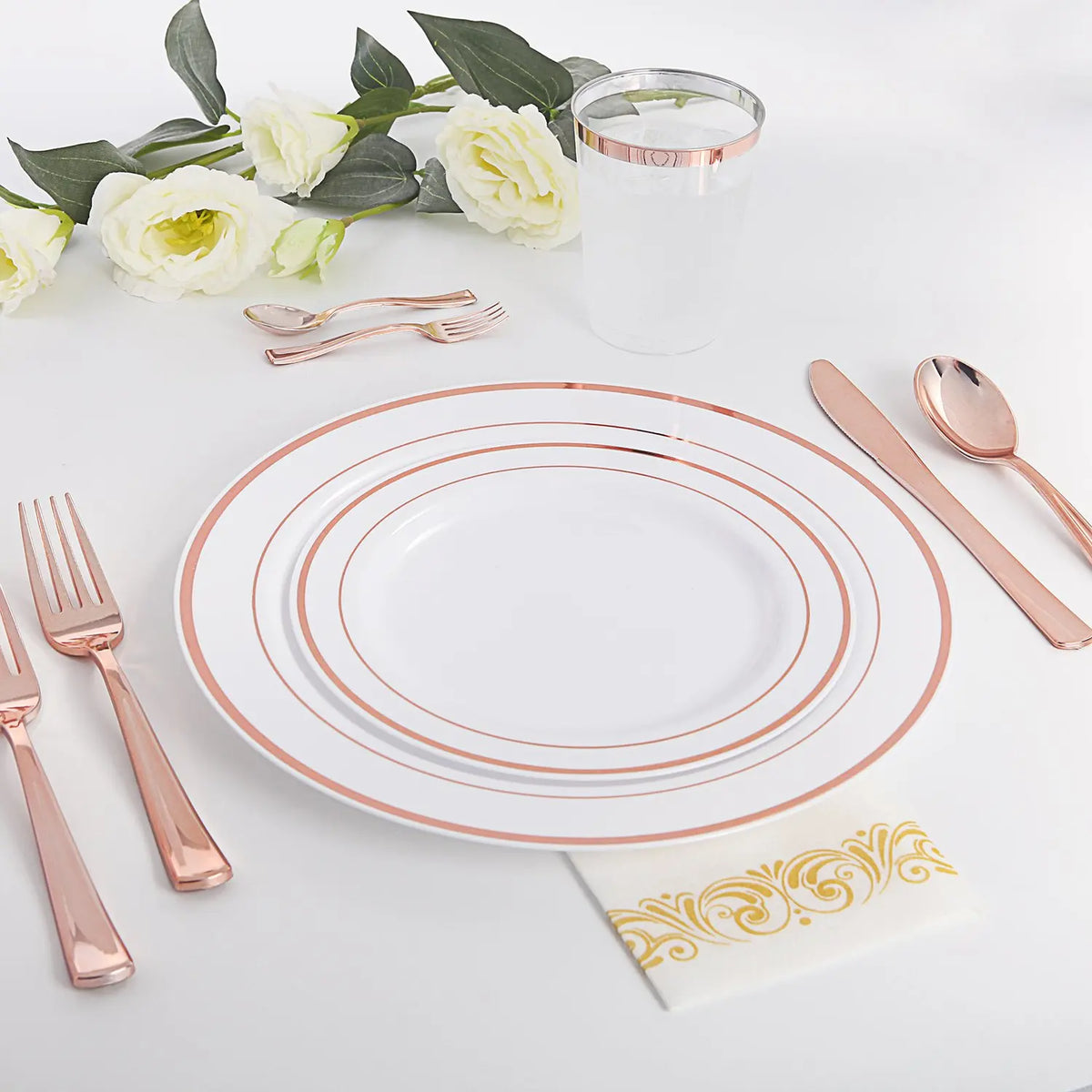 Ein Set elegante goldgerahmte Kunststoff-Essgeschirr, Besteck und ein Glas auf weißem Untergrund.