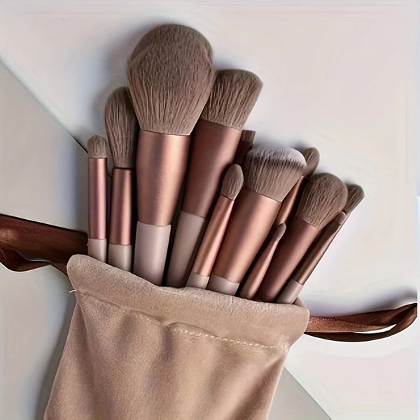 A set of luxury vegan makeup brushes in rose gold and nude tones displayed in a fabric pouch.