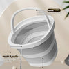 A white foldable plastic bucket with an arc handle is shown pouring water onto a flat base.