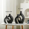 A display of three black ceramic vases of varying sizes on a white table.