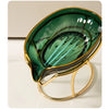 A glossy green leaf-shaped soap dish with a gold rim and stand.