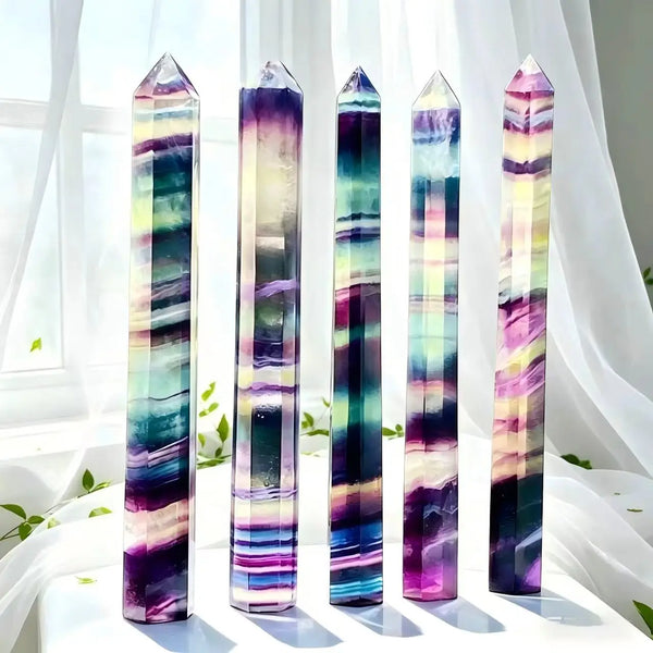 A collection of natural fluorite healing crystal wands in various shades of purple and green displayed on a white surface.