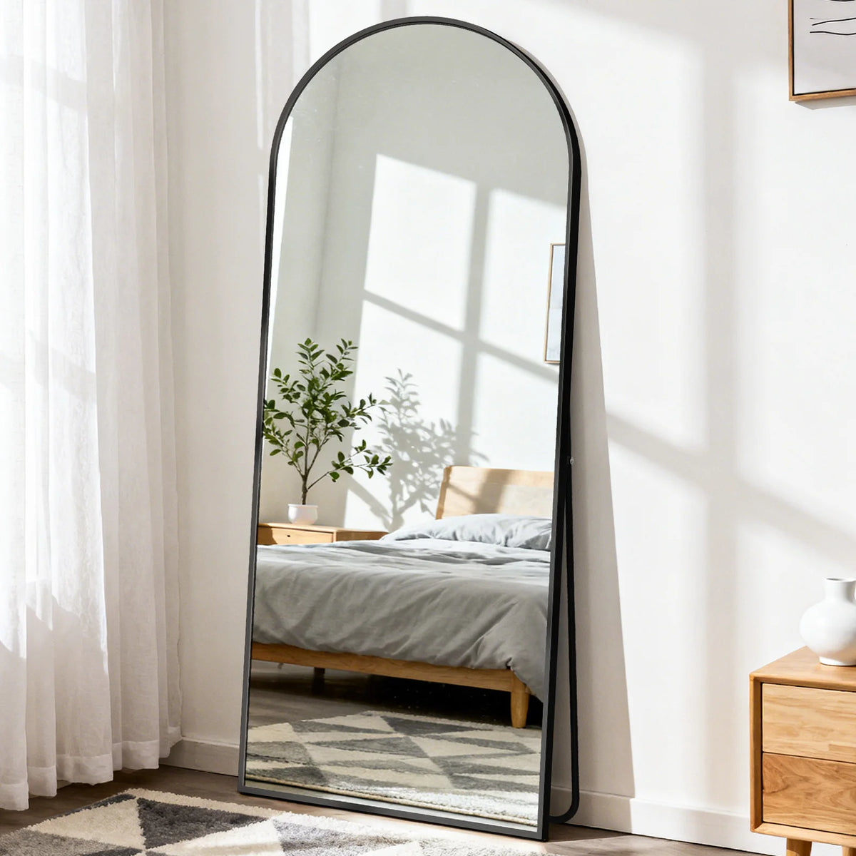 Langes ovales Spiegel mit schwarzem Rahmen, der ein Schlafzimmer-Interieur und Sonnenlicht reflektiert.