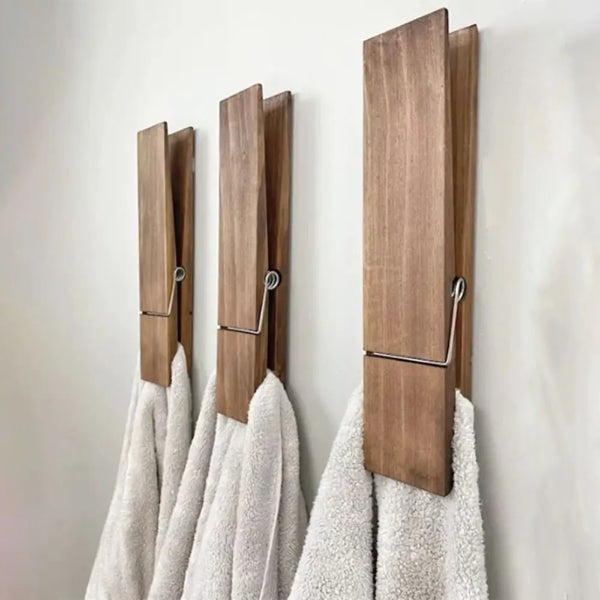A set of rustic wooden towel clips hanging on a white wall, with fluffy white towels visible below.