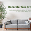 A gray sofa in a bright room with a large potted artificial olive tree and a wall sign encouraging decorating a green life.