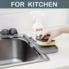 A hand is using a white dispenser bottle to clean food on a gray silicone sink mat and organizer.