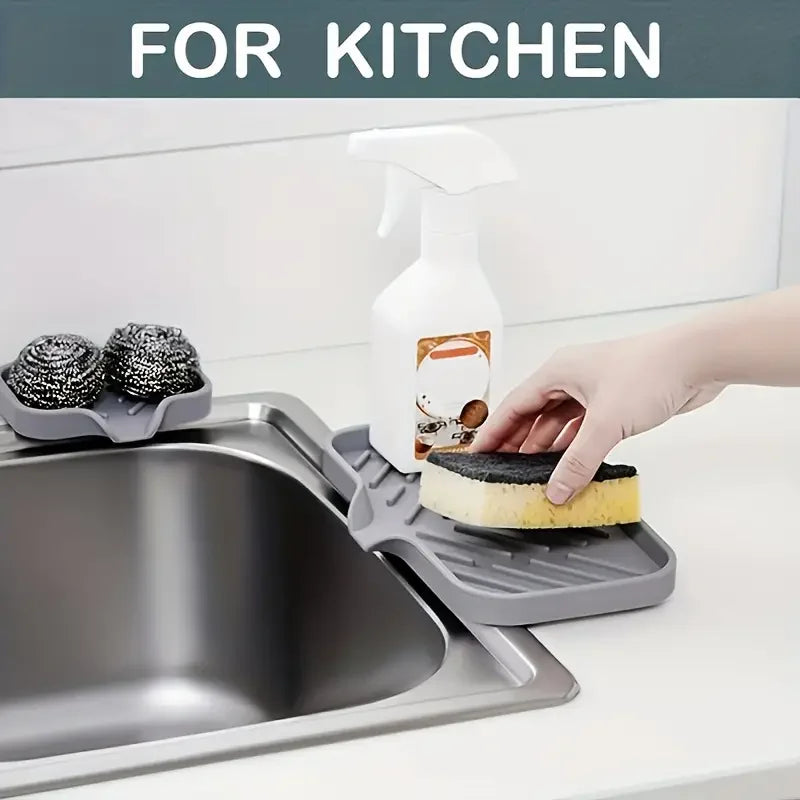A hand is using a white dispenser bottle to clean food on a gray silicone sink mat and organizer.