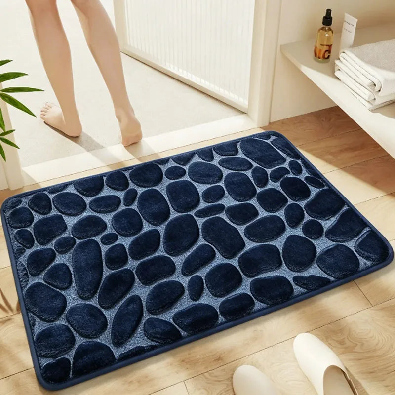 A dark blue, pebble-textured bathroom rug placed on a light wooden floor.