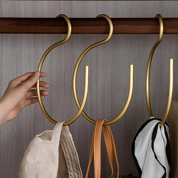 A hand is hanging a gold aluminum hat hook onto a wooden rack.