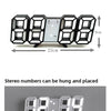 Schwarze 7-Segment-digitale Wanduhr mit weißer Anzeige und USB-Ladeanschluss an einer grauen Wand.