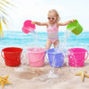 A young girl is splashing water from various colored plastic buckets onto the sand near the ocean.