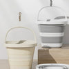 Two colors of a collapsible water bucket with handle for portable storage, cream and gray.