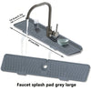 A large grey silicone faucet splash pad mat with a faucet and a glass cup shown in use.