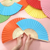 Une main ouvre un éventail pliable coloré en bambou et papier, montrant des nuances d'orange, jaune, vert et rose.