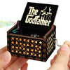 An antique wooden hand crank music box with a dark lid featuring the text The Godfather is held in a hand.