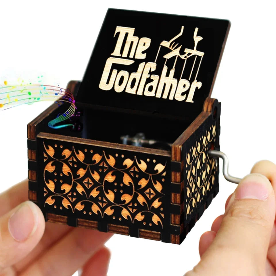 An antique wooden hand crank music box with a dark lid featuring the text The Godfather is held in a hand.