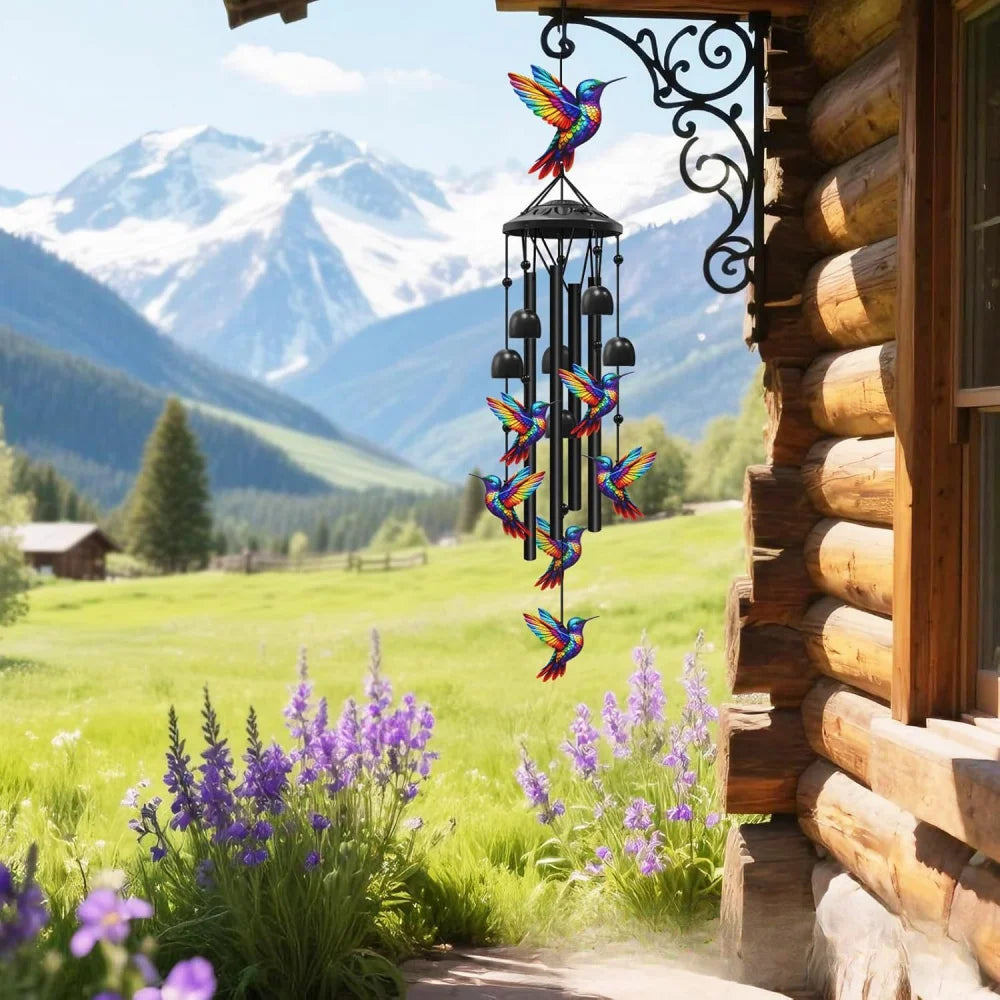 A handcrafted metal wind chime decoration hangs by a window, set against a scenic mountain landscape.