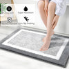 A person's legs are shown stepping onto a gray microfiber non-slip bath mat on a white floor.