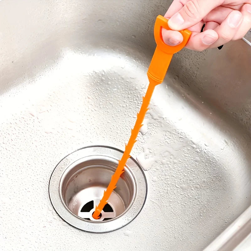 Una mano usa una herramienta flexible naranja para limpiar un desagüe de lavabo.