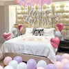 A celebration setup featuring pink and purple foil balloons spelling out Happy Birthday above a bed.