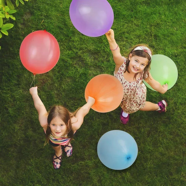 Two young girls are joyfully holding and playing with colorful latex balloons on a green lawn.