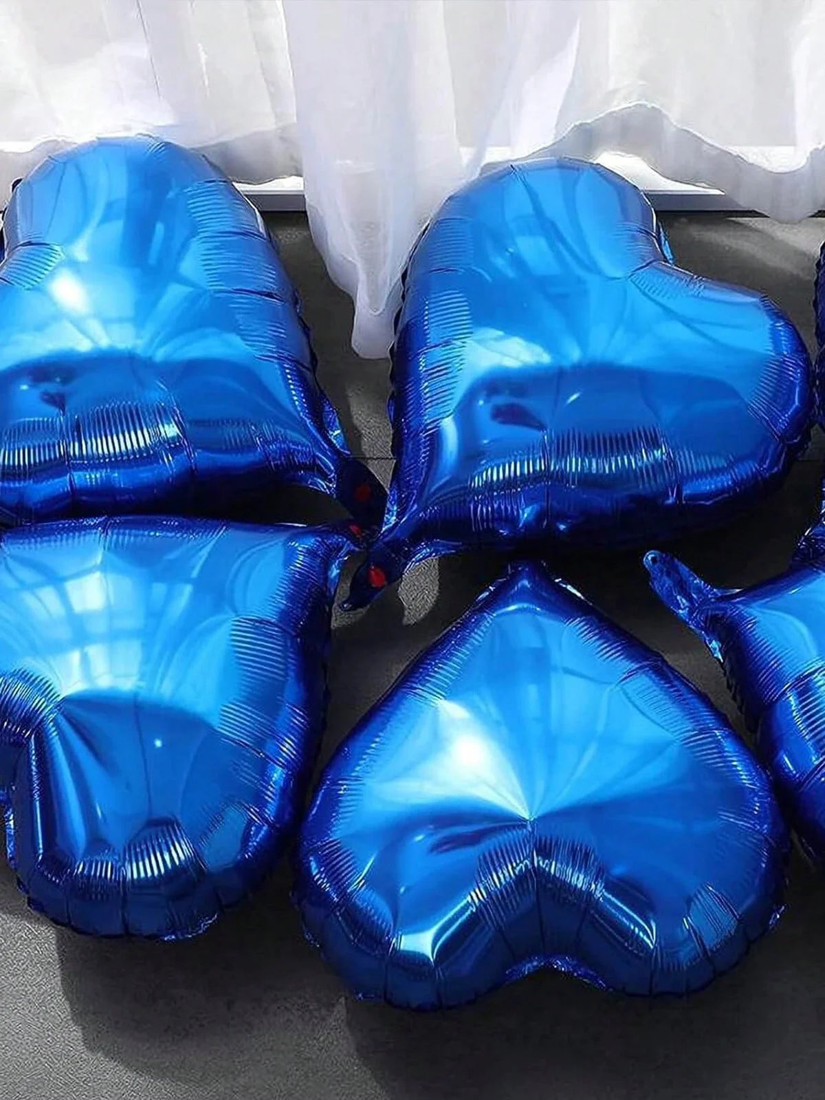 A set of shiny blue heart-shaped foil balloons displayed on a dark surface.