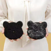 A pair of hands holds two black felt cat-shaped pet hair removers against a white background.