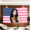 A woman posing in front of a large fabric banner featuring the American flag design with pink and white stripes.