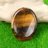 A polished, oval-shaped amber-colored quartz thumb stone resting on bright green grass.