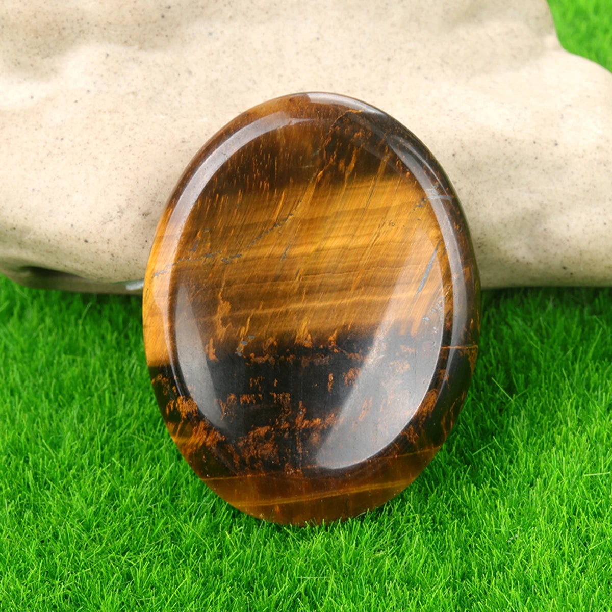 A polished, oval-shaped amber-colored quartz thumb stone resting on bright green grass.