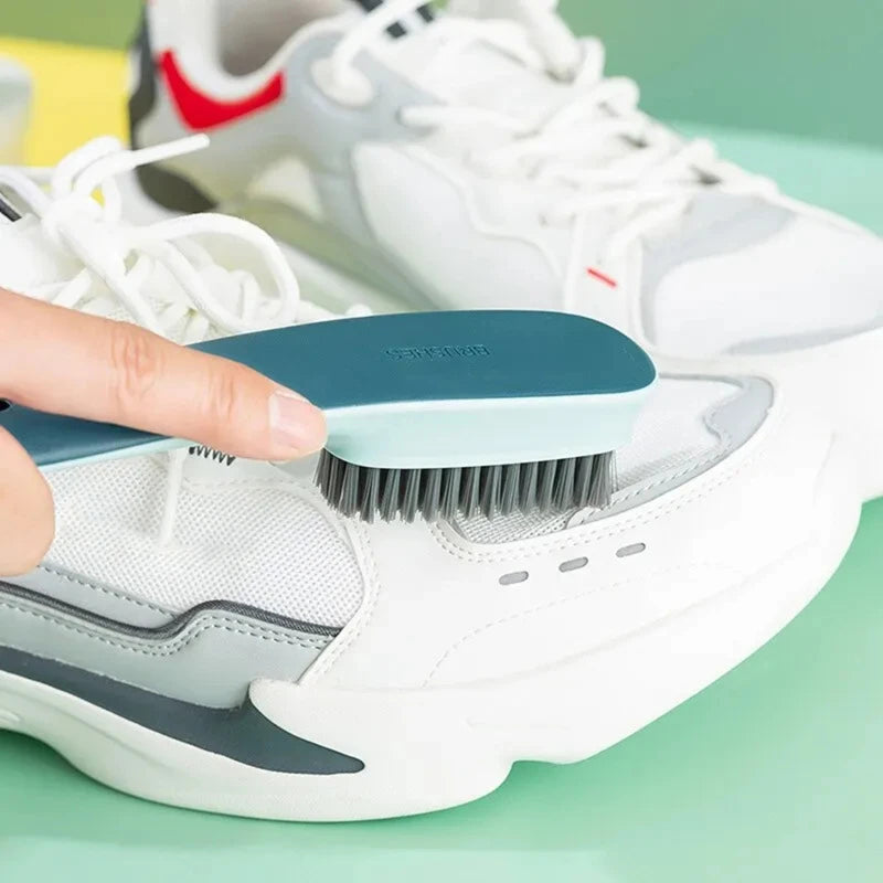 Une main utilise une brosse bleue de nettoyage sur une chaussure de sport blanche pour nettoyer la surface.