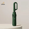 A dark green windproof automatic folding umbrella standing upright on a white surface.