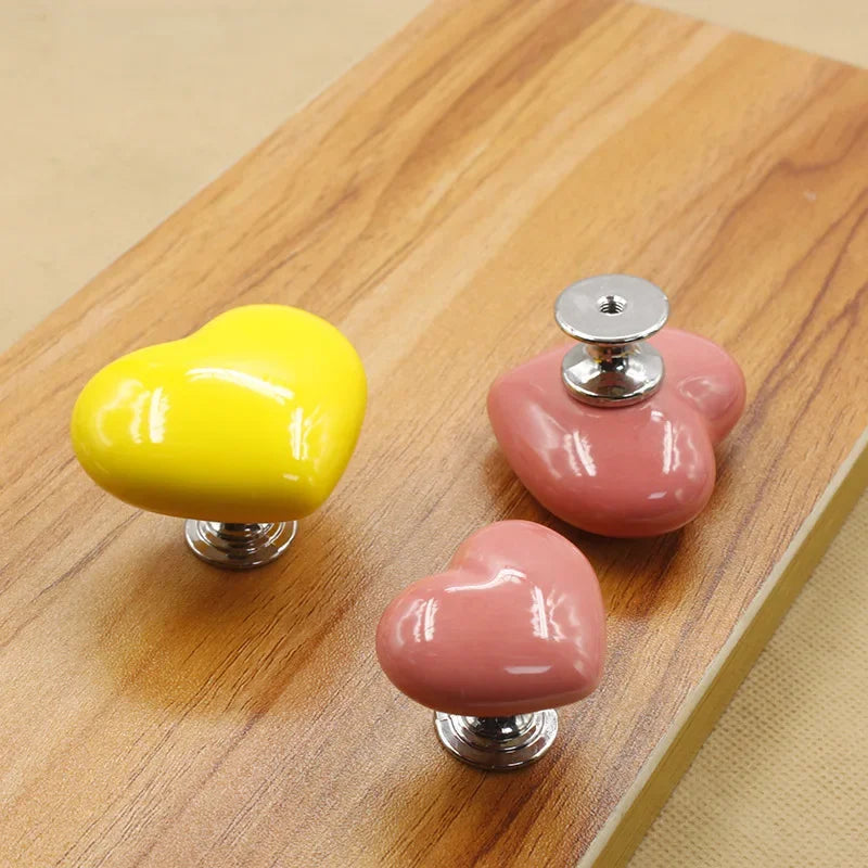 Trois boutons de chasse d'eau en forme de cœur, jaunes et roses, posés sur une surface en bois.