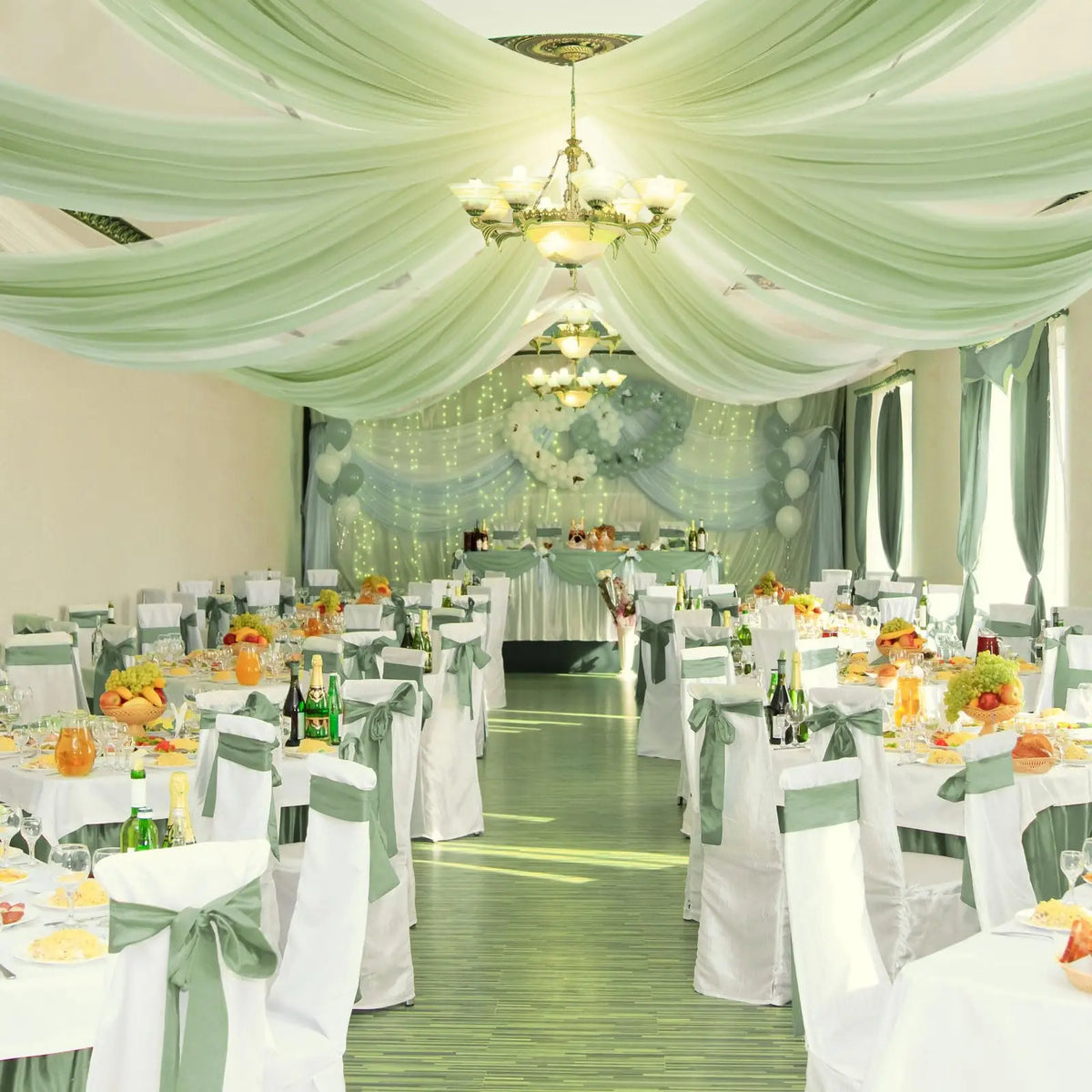 Elegant event hall decorated with sheer sage green chiffon draping and white tables