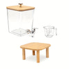 A clear glass and wooden laundry detergent dispenser with a stainless steel pump and a measuring cup.