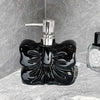 A black ceramic pump dispenser bottle with a bowknot design and silver pump mechanism on a gray stone surface.